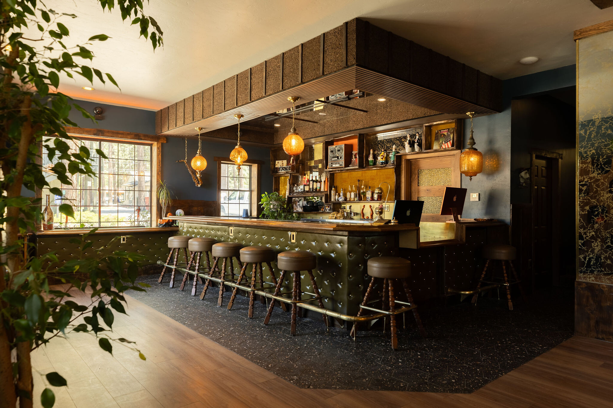 The Burgundy bar — green tufted leather base with brass-topped counter and amber swag pendants