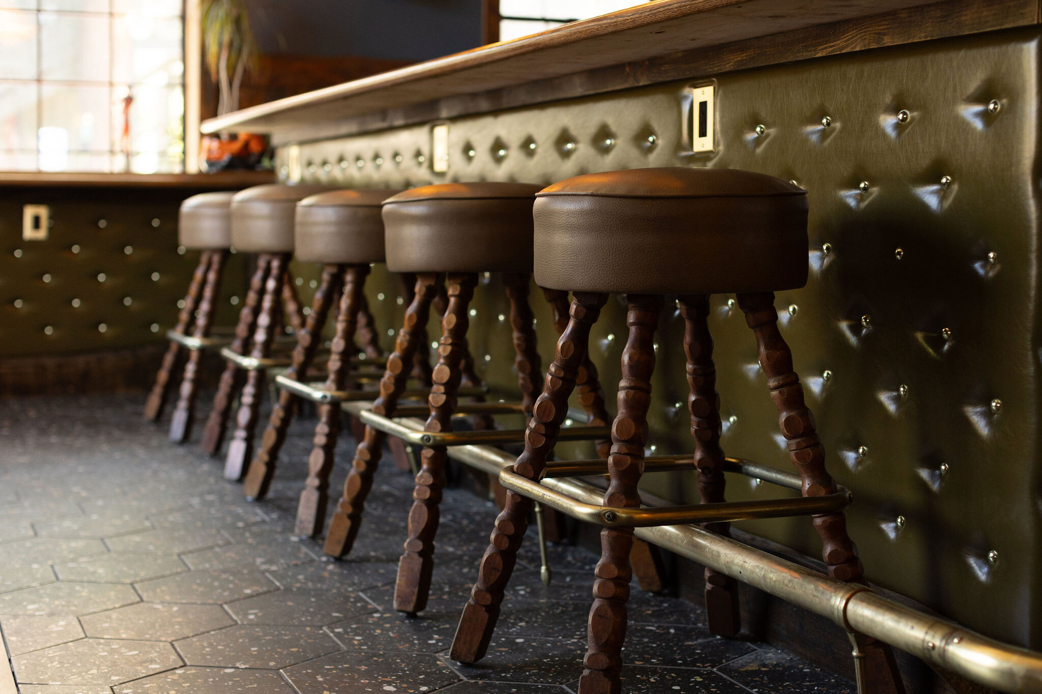 Close-up of leather-topped wood spool bar stools at the brass-rail bar