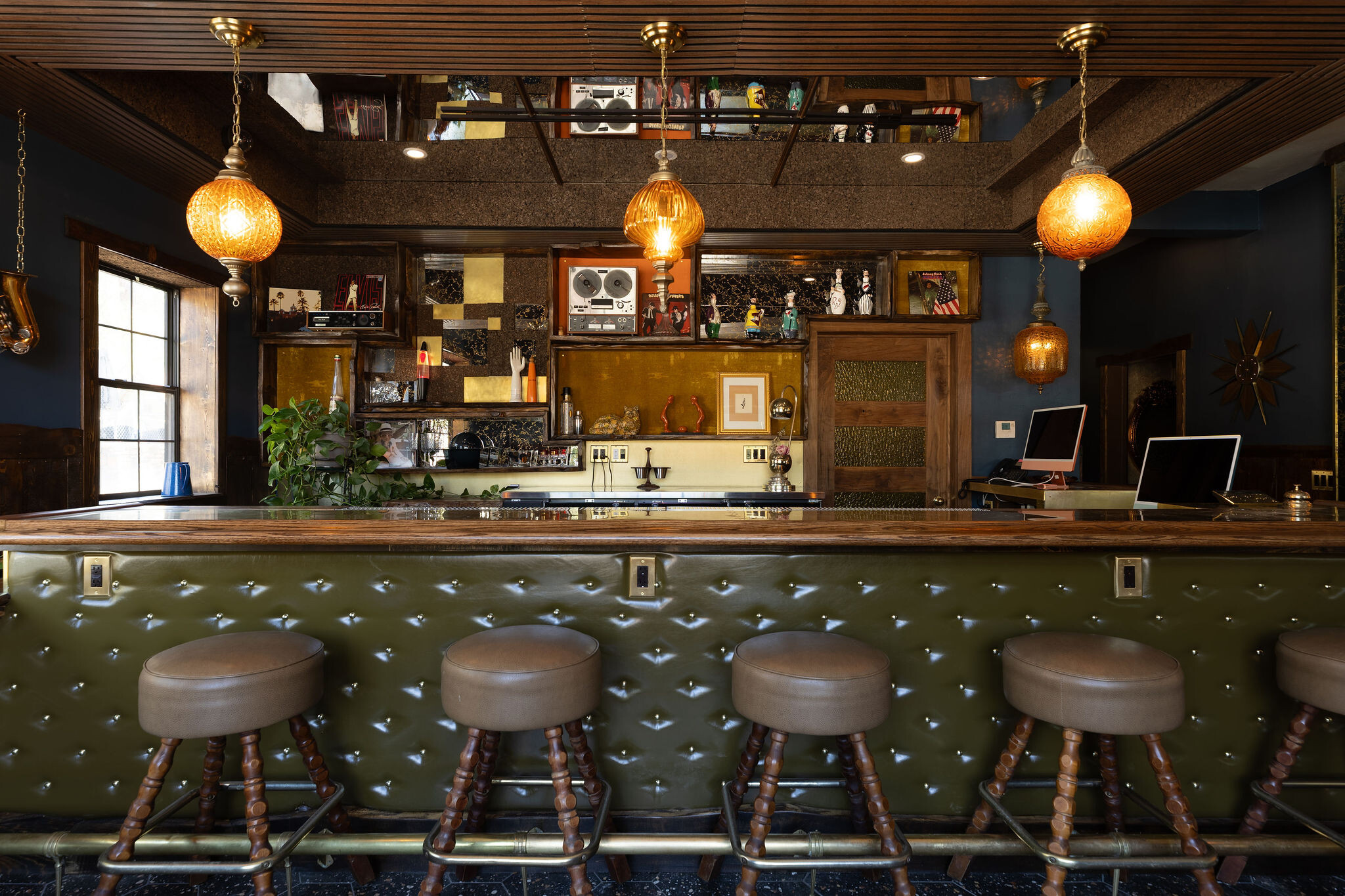 Five wood spool bar stools at the green tufted leather bar