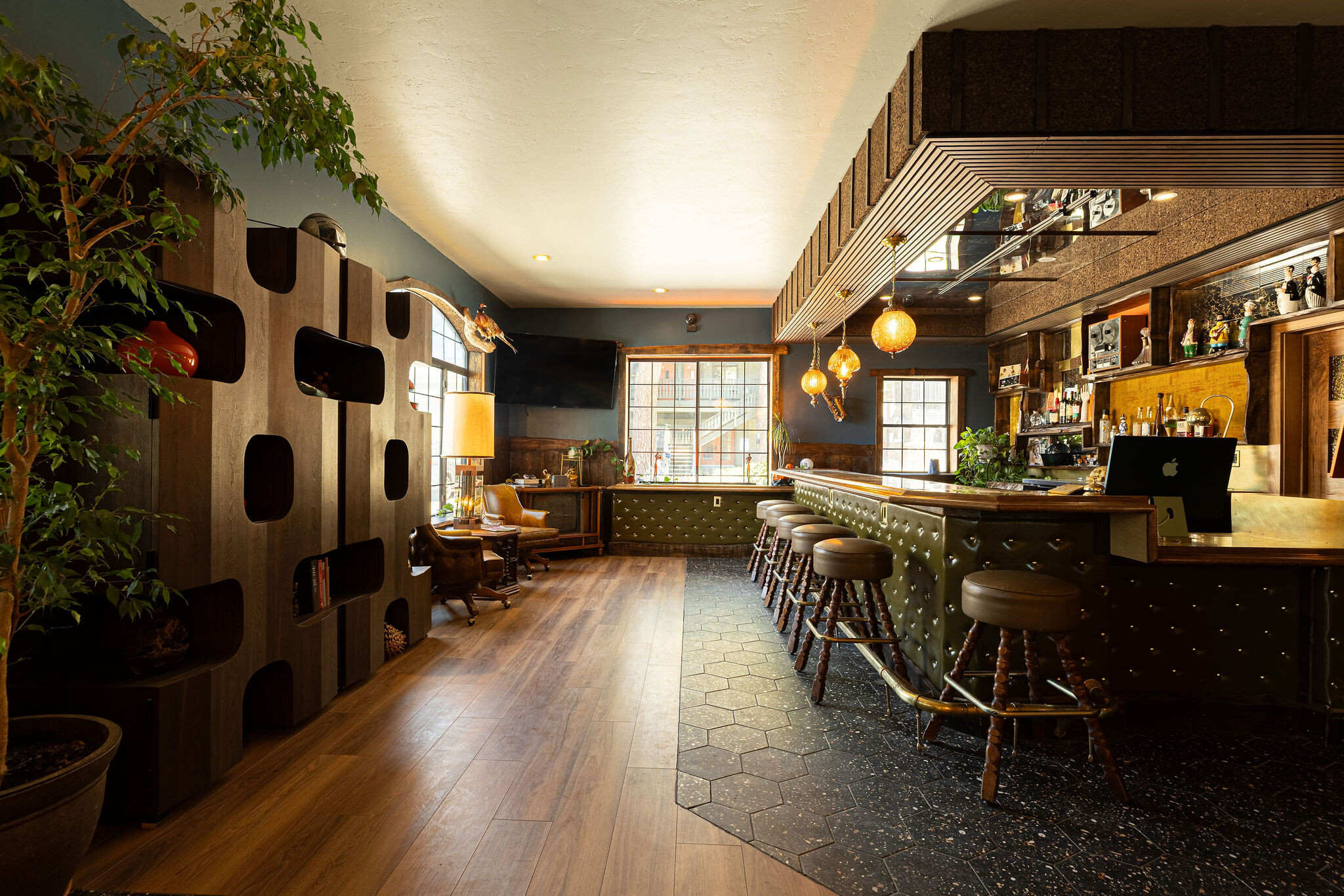 Three amber swag pendants over the green tufted leather bar, plant in foreground