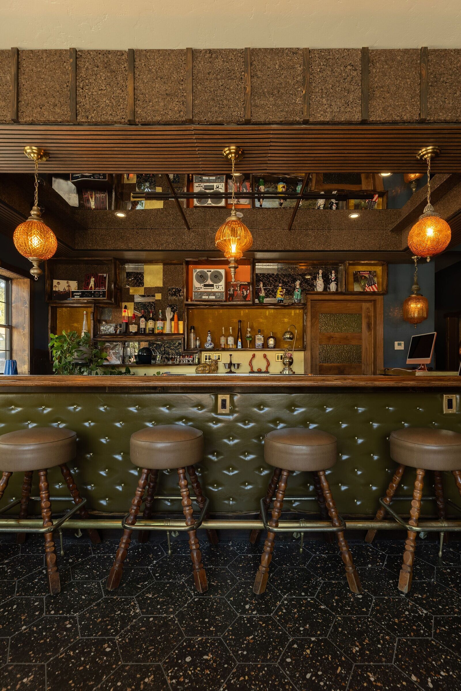 Detailed front view of the bar with three amber globe pendants over the green tufted base